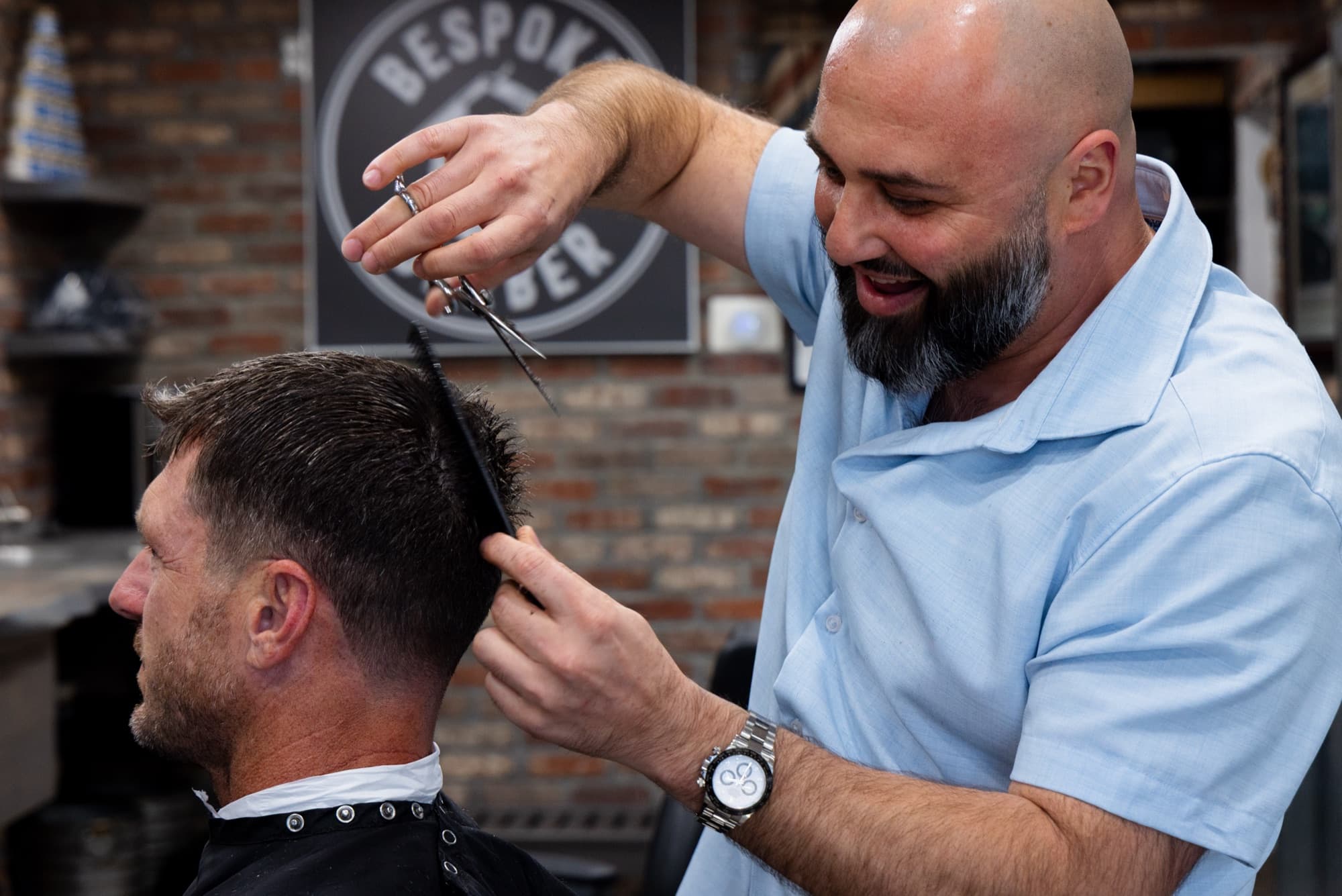 Boris Baybachayev smiling mid-cut with scissors raised at Bespoke Barber